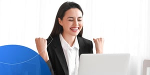 woman sitting at desk with closed eyes and hands in fists celebrating in front of laptop