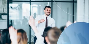 Man standing in front of crowd and pointing at someone in the audience with their hand raised