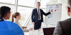 man pointing to statistics on white board in a meeting room 