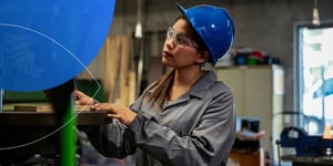 woman wearing blue helmet and lab glasses inspecting something