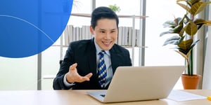 man wearing suit explaining something to his laptop and smiling