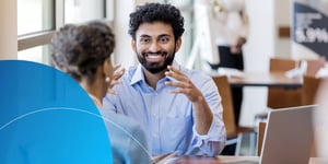  man sitting down with hand gesture smiling at woman in front of him