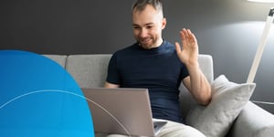 man waving to his laptop sitting on a sofa 