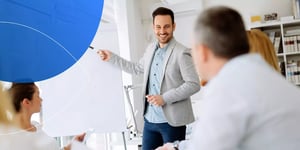  man pointing at white board and smiling to people in front of him