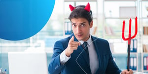 man in suit with devil horns and devil stick pointing at camera looking angry