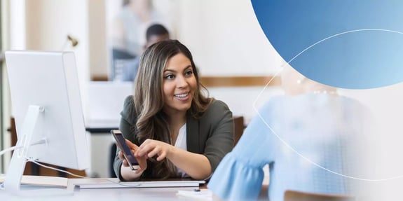  woman pointing to her phone explaining and smiling to woman in front of her 