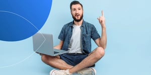 man sitting crossed legged on the floor one hand pointing up and laptop on his knee